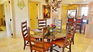 A dining area with a round glass table surrounded by wooden chairs with leather cushions.