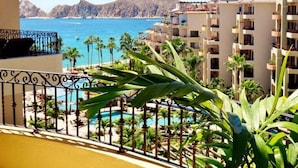 A hotel balcony with a view of a pool, palm trees, and a mountain in the background.