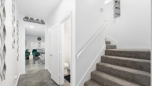 A clean, modern hallway with a staircase leading to a second floor. A 'WELCOME' sign hangs on the wall, and a door is visible on the left. - Contemporary-3 Bedroom-Rooftop in the Heart of Downtown Conroe (Conroe)