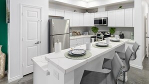A modern kitchen with white cabinetry, a stainless steel refrigerator, a microwave, and a central island with chairs. - Contemporary-3 Bedroom-Rooftop in the Heart of Downtown Conroe (Conroe)