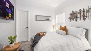 A modern bedroom with a bed, a wall-mounted TV displaying streaming services, a decorative mirror, and a unique wall art piece. - Contemporary-3 Bedroom-Rooftop in the Heart of Downtown Conroe (Conroe)