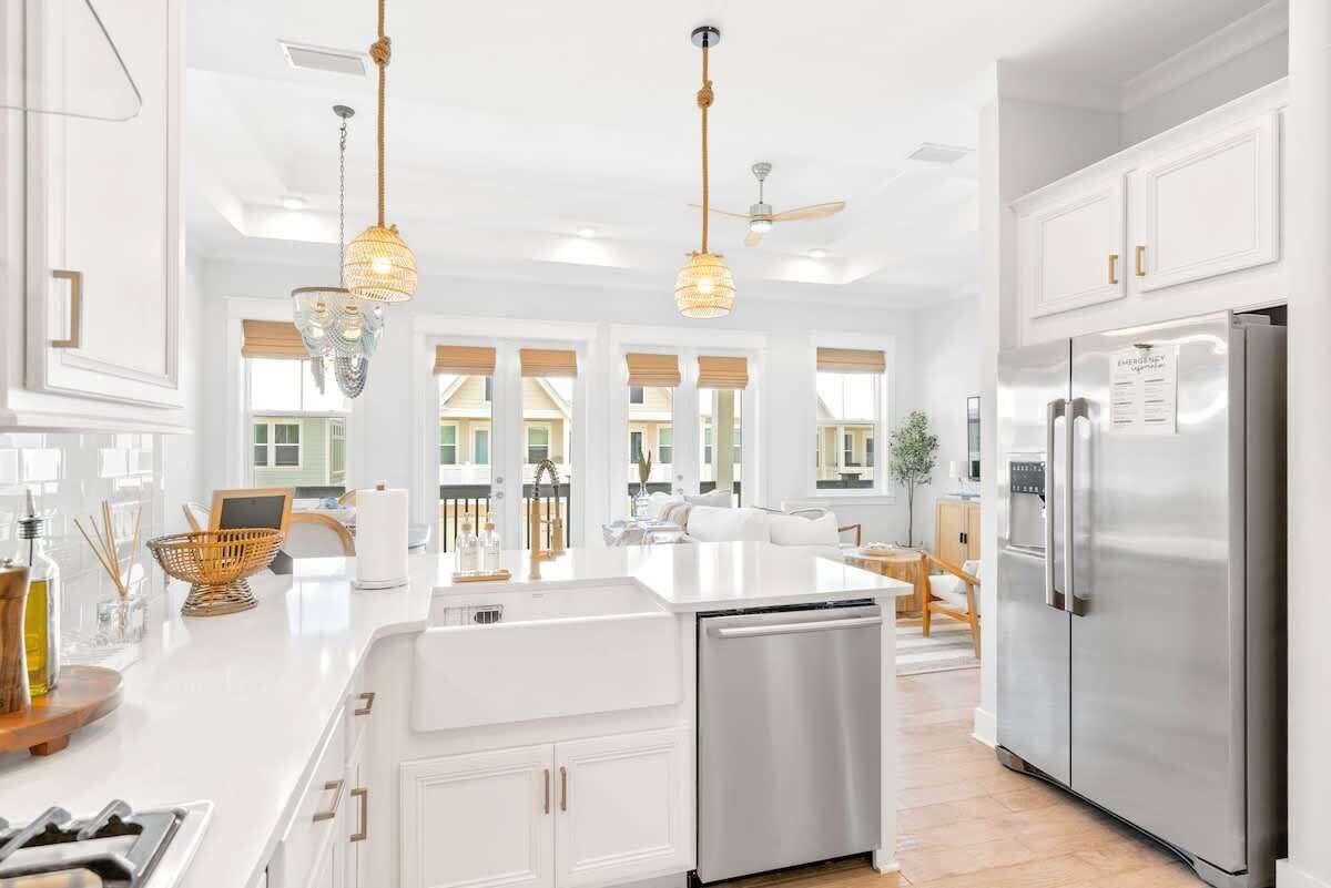 Une cuisine moderne avec des meubles blancs, des appareils en acier inoxydable et des luminaires suspendus.