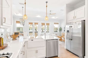 Une cuisine moderne avec des meubles blancs, des appareils en acier inoxydable et des luminaires suspendus.