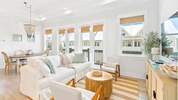 A bright living room with a white sofa, wooden coffee table, and a dining area with a table and chairs. - Watersound Escape by Stay on 30a (Inlet Beach)