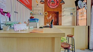 A reception area with a wooden counter, a desk with a computer, a clock, and a sign indicating an office. - Hotel O Harwin Homestay (Batu)