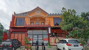 A two-story building with a red and orange facade, a balcony, and a large window. - Hotel O Harwin Homestay (Batu)