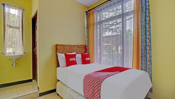 A hotel room with a bed, a window with curtains, a sink, and a door. - Hotel O Harwin Homestay (Batu)