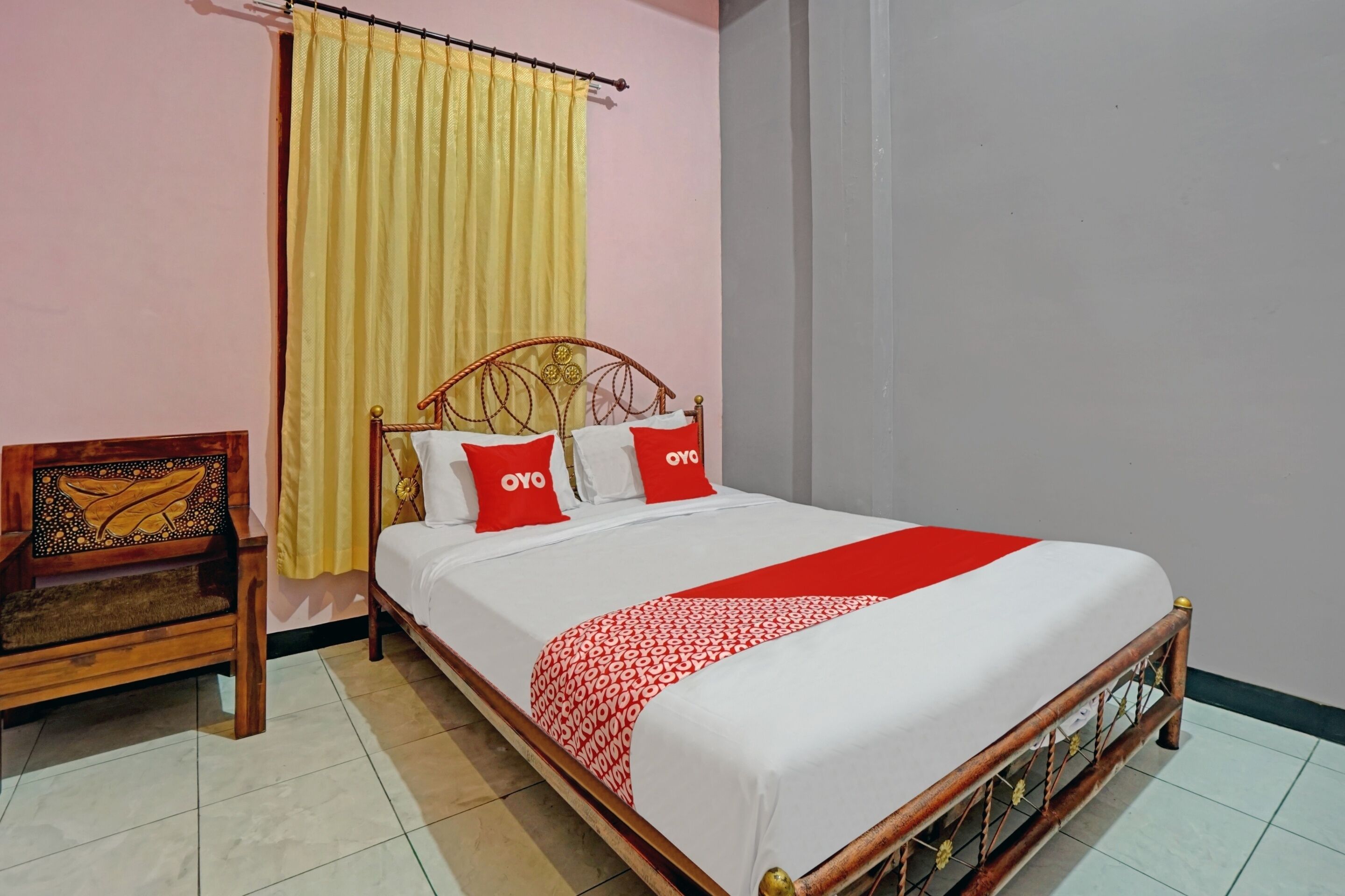 A neatly made bed with a red and white bedspread, a wooden headboard, and two red pillows with "OYO" on them.