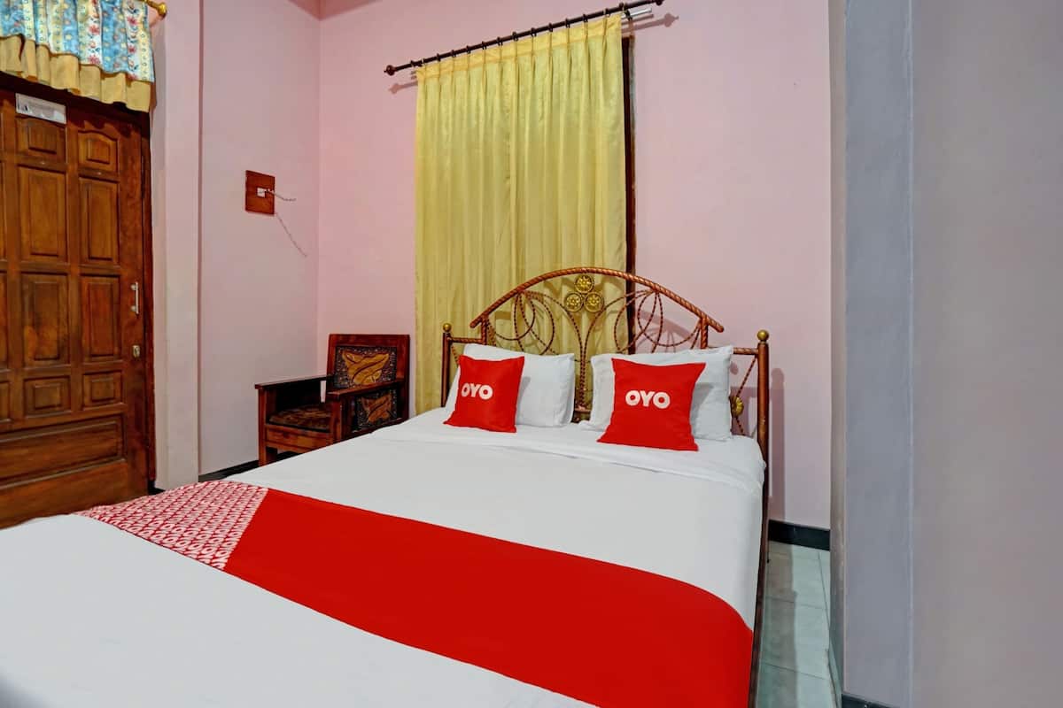 A bedroom with a wooden bed, red and white bedding, a yellow curtain, and a wooden wardrobe.