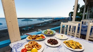 A table with various dishes, a beach view, and outdoor seating with umbrellas. - Villa Petra in Afrato (Kefalonia)