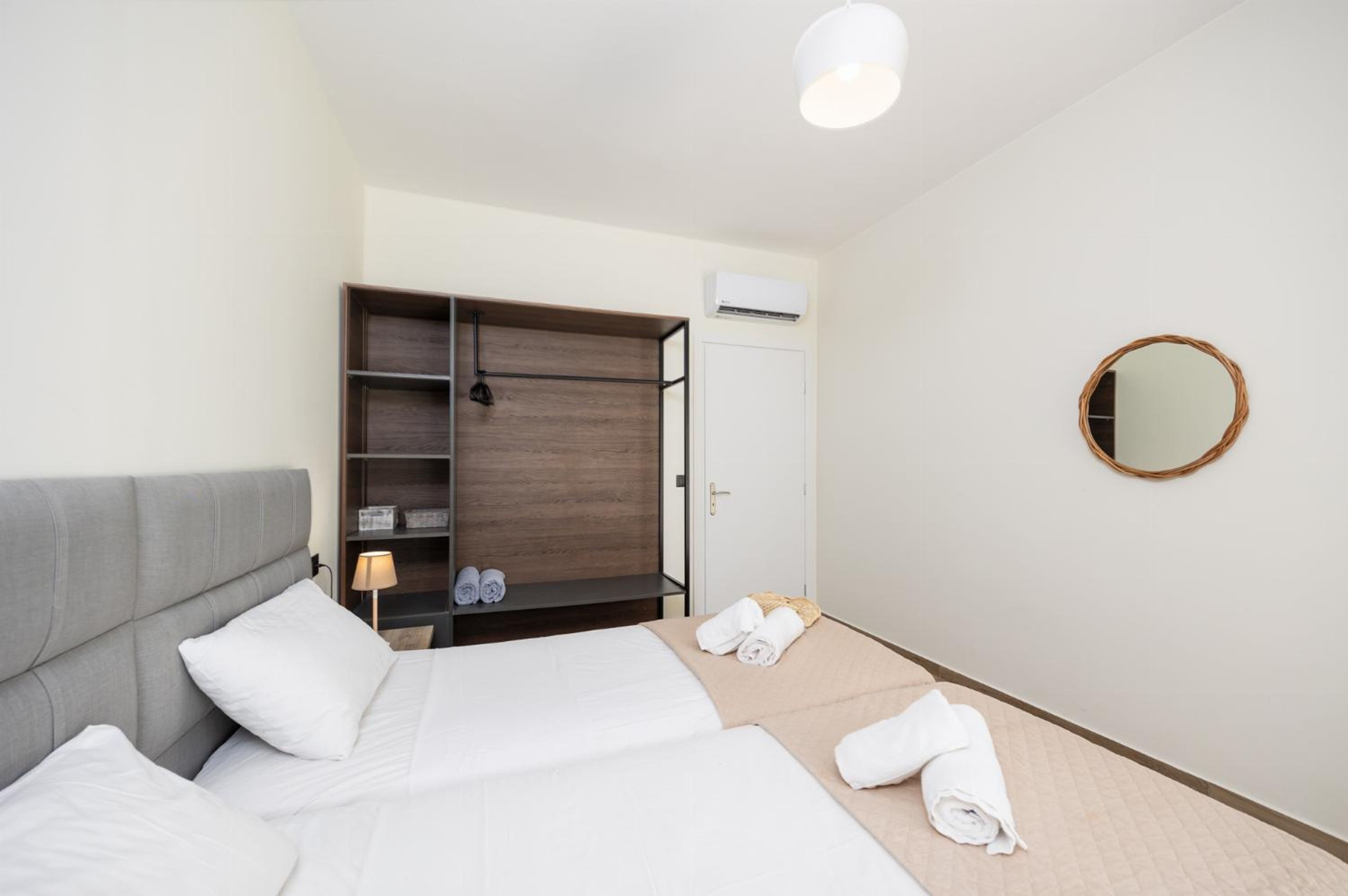 A hotel room with a bed, a wardrobe, a mirror, and a small table with a lamp.