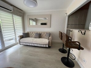 Un salon comprenant un canapé, une table basse et un téléviseur. Une porte-fenêtre coulissante donne accès à un balcon.