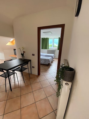 Een kamer met een eettafel, stoelen, een potplant, een bed met raam en een radiator.