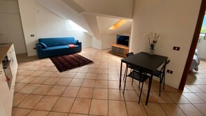 Un espacio habitable compacto con kitchenette, un sofá azul, una mesa de comedor con sillas y un televisor.