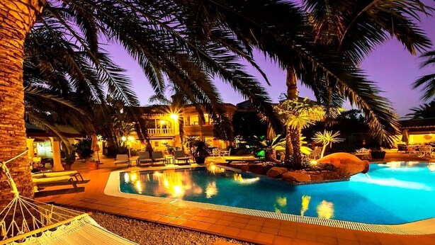 A swimming pool surrounded by palm trees and lounge chairs, with a hammock and a building in the background. - Villa 'Luxury Xenofilia Lll' with Mountain View, Wi-Fi and Air Conditioning (Moraira)
