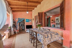 A dining area with a table set for four, wooden chairs, a wooden ceiling, and a kitchen in the background.