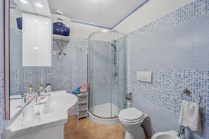 Un baño con ducha envuelta en vidrio, un lavabo blanco, un inodoro y un espejo.