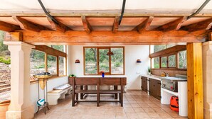 A covered outdoor kitchen with a wooden bench, a table, and a view of the outdoors.