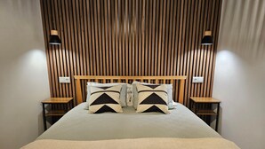 Una cama con cabecera de madera, dos mesitas de noche y dos lámparas de pared.