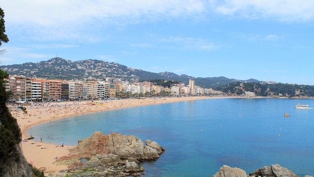 A coastal cityscape with a beach, buildings, and rocky outcrops.