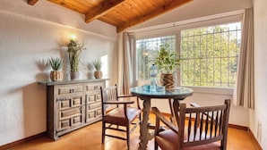 A dining area with a wooden table and chairs, a cabinet with decorative plants, and a window with a view of trees.