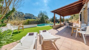 A poolside area with lounge chairs, a pergola, and a view of the pool and surrounding greenery.