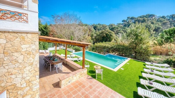 A pool with a pergola, outdoor seating, and a stone wall.