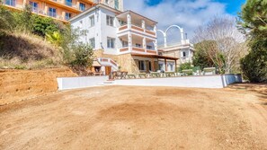 A multi-story building with balconies, a patio area with outdoor seating, and a dirt driveway.