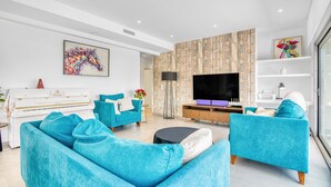 A modern living room with a piano, teal sofas, a flat-screen TV, and a decorative wall. - Villa "Modern Seaview" with Private Pool & Wi-Fi (Benitachell)