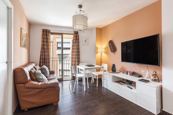 A modern living room with a sofa, dining table, chairs, a flat-screen TV, and a fireplace.