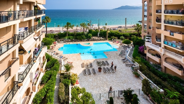A hotel with a swimming pool, lounge chairs, and a view of the beach. - Apartment "Palme d'Or" with Sea View, Shared Pool & Wi-Fi (Cannes)