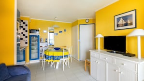 A compact living space with a dining area, kitchenette, and a television on a cabinet. - Apartment "Palme d'Or" with Sea View, Shared Pool & Wi-Fi (Cannes)