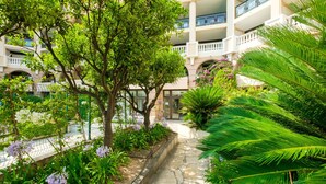 A courtyard with a stone pathway, lush greenery, and a building with multiple balconies. - Apartment "Palme d'Or" with Sea View, Shared Pool & Wi-Fi (Cannes)