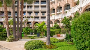 A hotel courtyard with palm trees, well-maintained greenery, and a multi-story building with balconies. - Apartment "Palme d'Or" with Sea View, Shared Pool & Wi-Fi (Cannes)