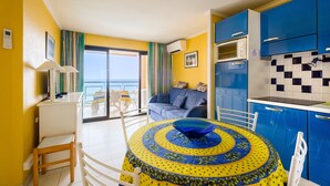 A room with a dining table, a sofa, and a kitchen area with blue cabinets. - Apartment "Palme d'Or" with Sea View, Shared Pool & Wi-Fi (Cannes)