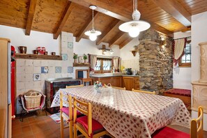 Una cocina rústica con vigas de madera, pared de piedra y un comedor con una mesa preparada para cuatro.