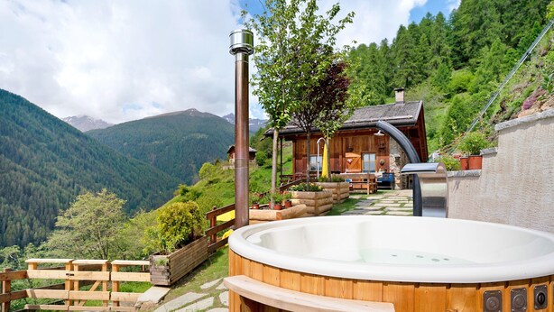 Un jacuzzi de madera con un sendero de piedra que lleva a una cabaña de madera en una zona montañosa.
