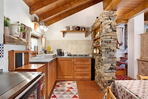 A kitchen with wooden cabinets, a stone wall, and a tiled backsplash.