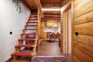 A wooden staircase with red patterned steps leading to a kitchen area with wooden cabinets and a dining table.