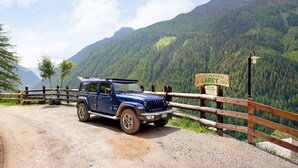 Un SUV azul estacionado junto a una cerca de madera con un cartel que indica un sendero de senderismo.
