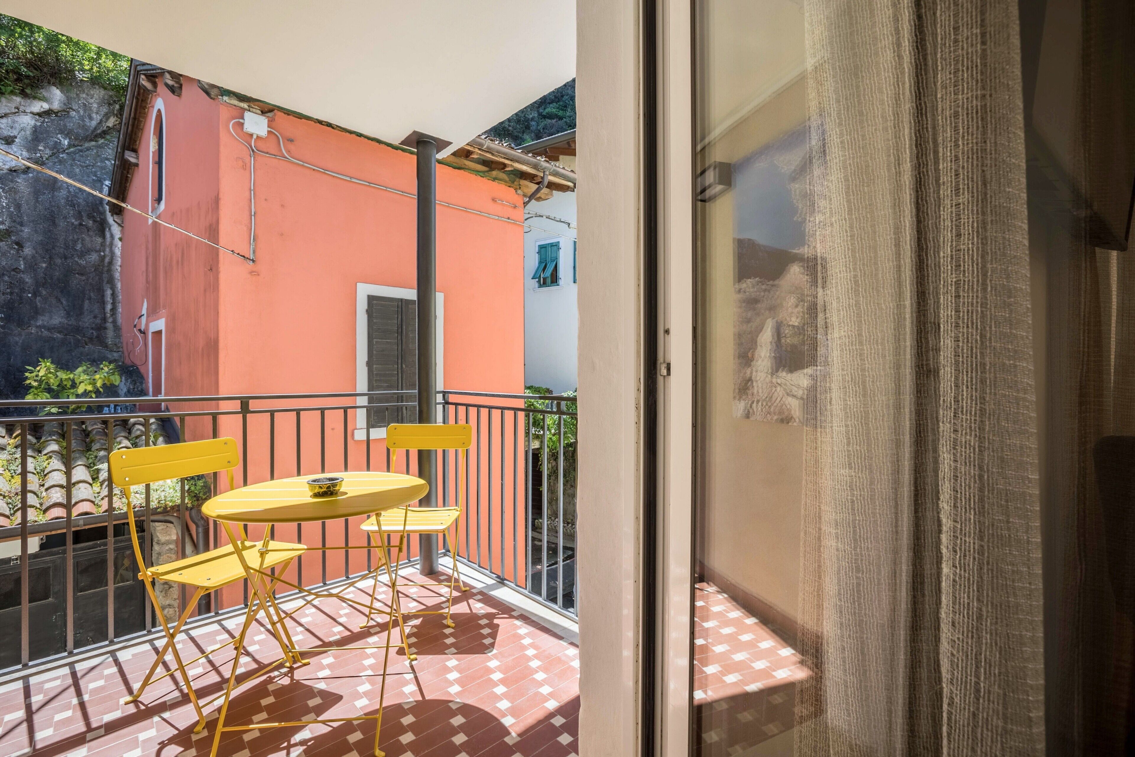 A balcony with a checkered floor, yellow chairs, and a small round table.