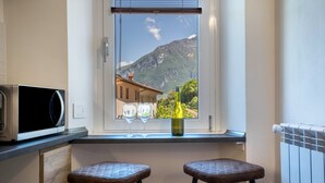 A kitchen with a microwave, two stools, a wine bottle, and glasses on a window sill with a mountain view. - Apartment "Casa Chiarani" with Mountain View, Balcony and Wi-Fi (Arco)