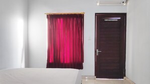 Een hotelkamer met een bed, een rood gordijn, een houten deur en een lichtschakelaar aan de muur.
