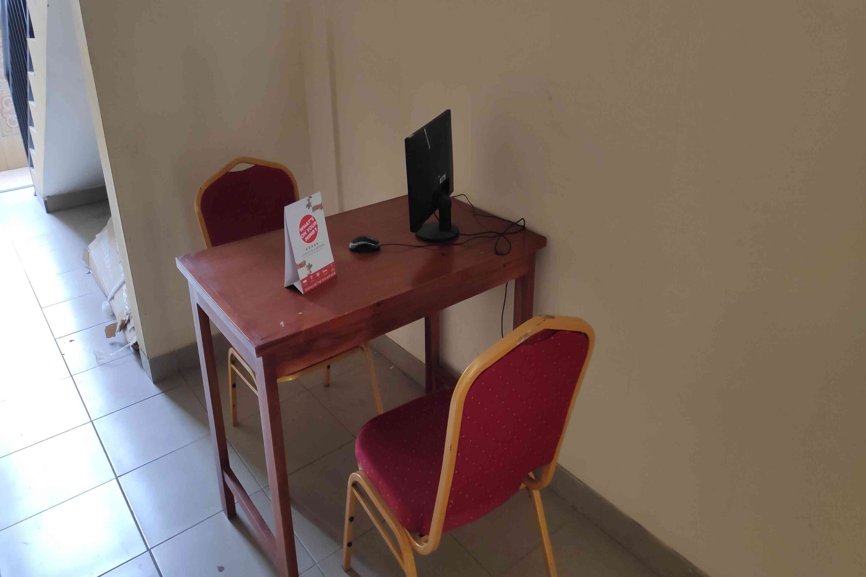 A small office space with a wooden desk, a computer monitor, a red chair, and a white bag on the desk.