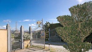 A gated entrance with a sign, a paved pathway, and a tree.