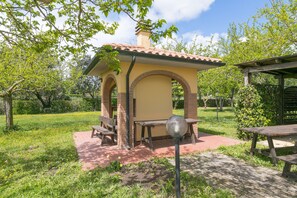 Un pequeño pabellón al aire libre con un arco de ladrillo, una mesa y bancos.