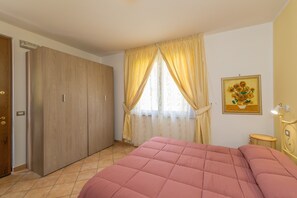 Un dormitorio con cama, armario, ventana con cortinas y un cuadro en la pared.