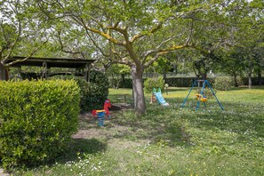 Un parque con un columpio, un tobogán y una zona de estar cubierta.