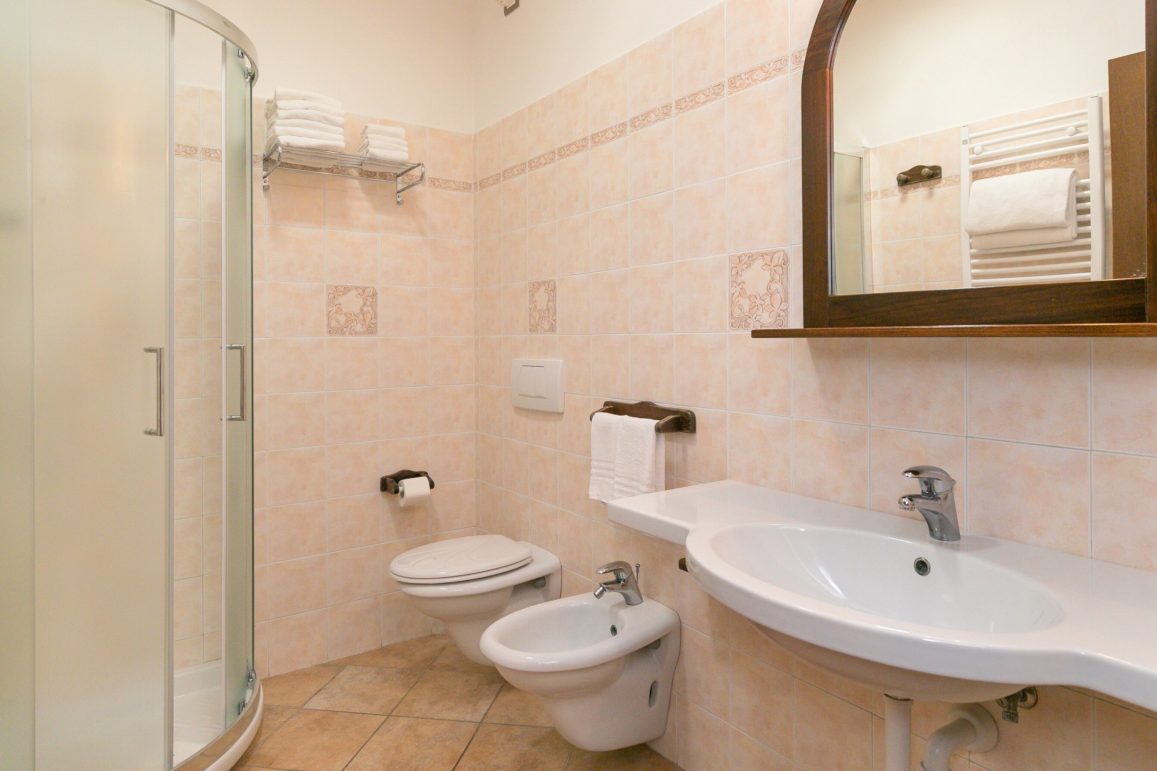 Un baño con cabina de ducha de vidrio, inodoro, bidé y lavamanos con espejo superior.