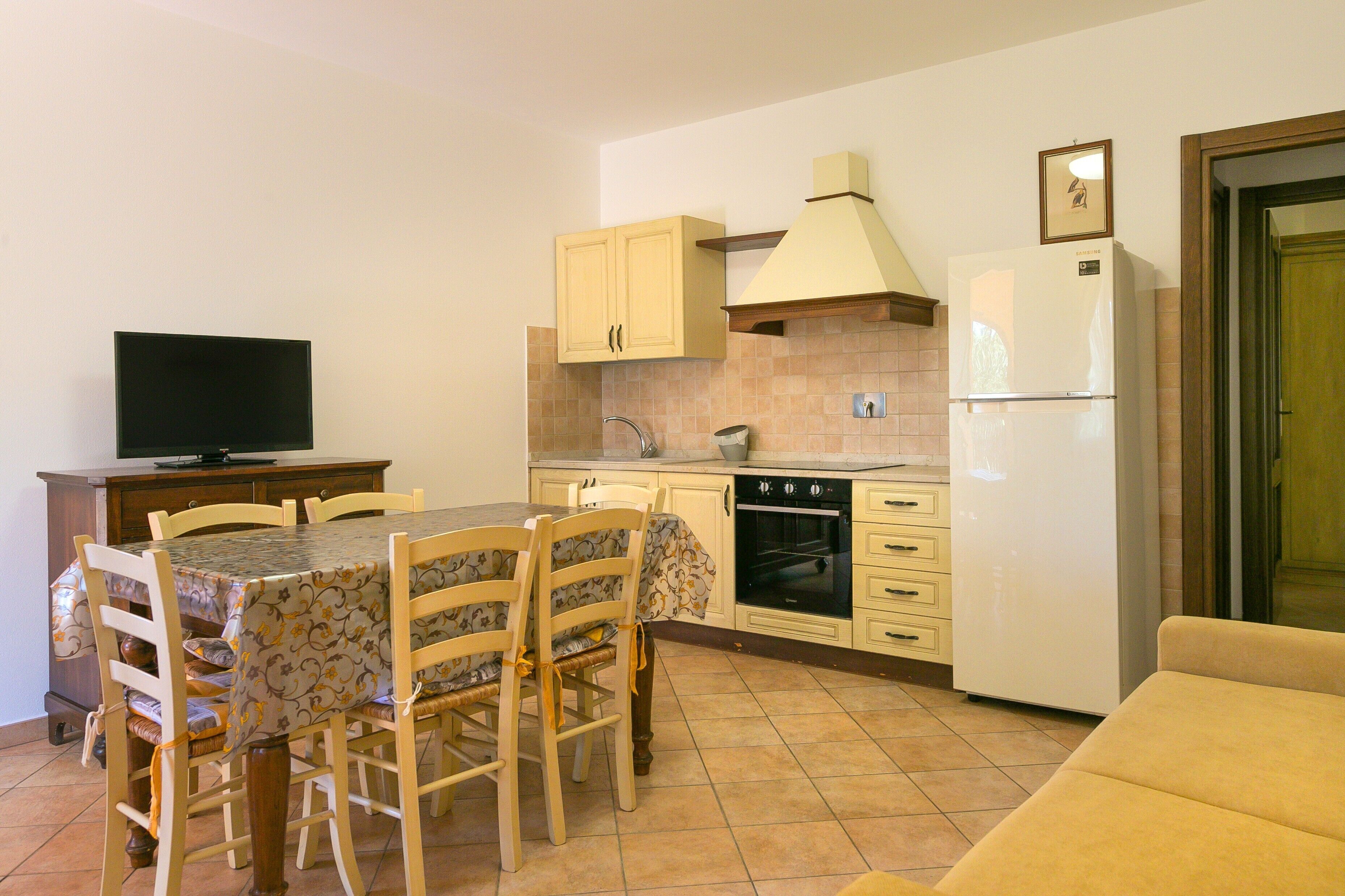Una cocina compacta con una mesa de comedor, sillas, televisor, refrigerador y sofá.